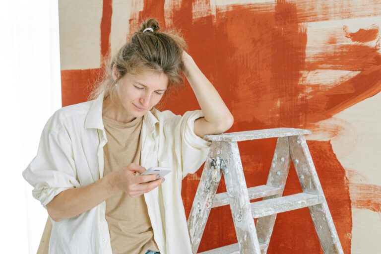 Woman in White Button Up Shirt Leaning on a Stepladder Using Cellphone