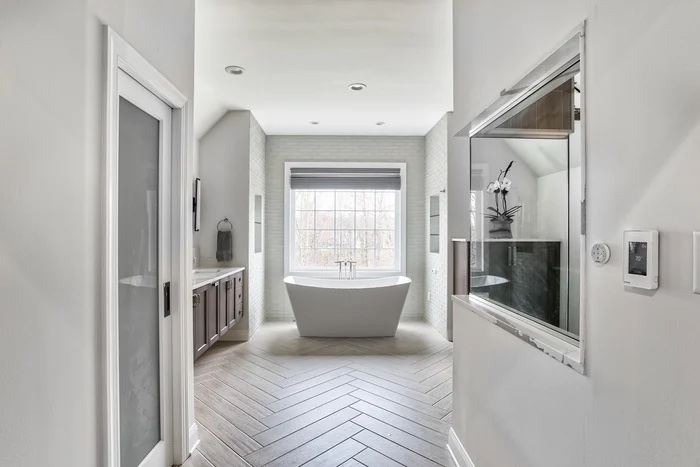 Modern spa-style bathroom renovation with freestanding tub, chevron-patterned tile floor, and large window — designed by KraftMaster Renovations and featured by MrSteam.
