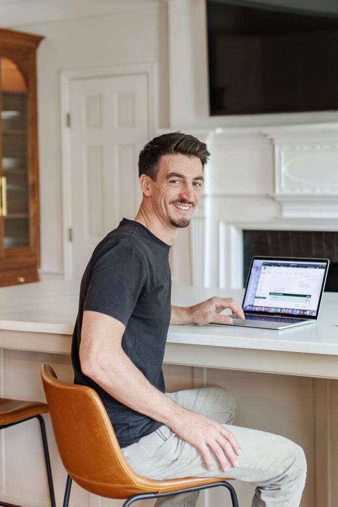 Chris Stevens, project manager at KraftMaster Renovations, working at a laptop in a kitchen setting.
