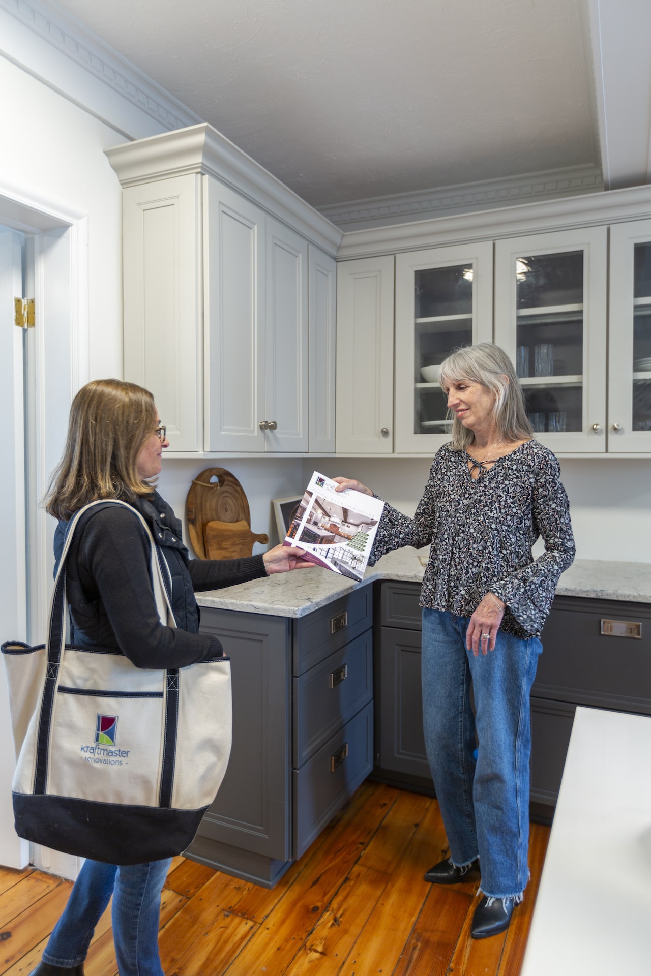 Woman hands brochure to client in a modern kitchen showroom