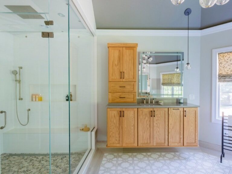 Modern bathroom renovation with light wood cabinetry, frameless glass shower, and custom tile floor — designed by KraftMaster Renovations in Chatham, NJ.