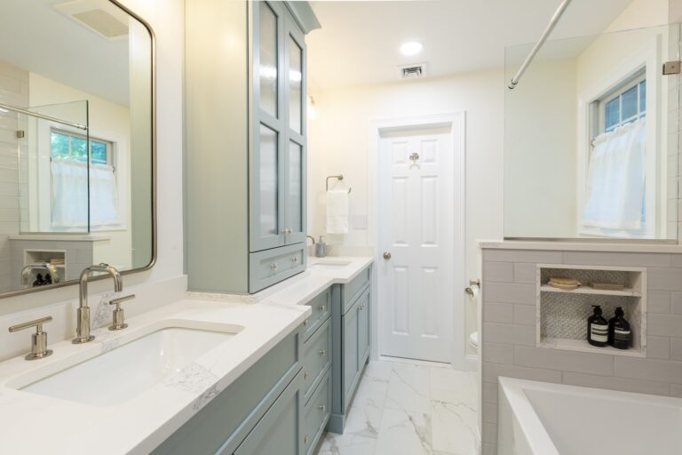 Modern hall bathroom with soft blue cabinetry, quartz counters, recessed shower niche, and elegant storage — remodeled by KraftMaster Renovations in NJ.