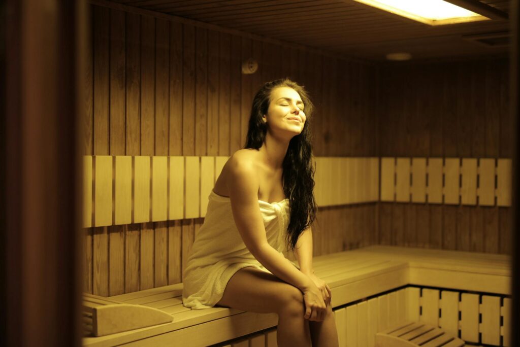 Woman relaxing in a wooden sauna, wrapped in towel, eyes closed