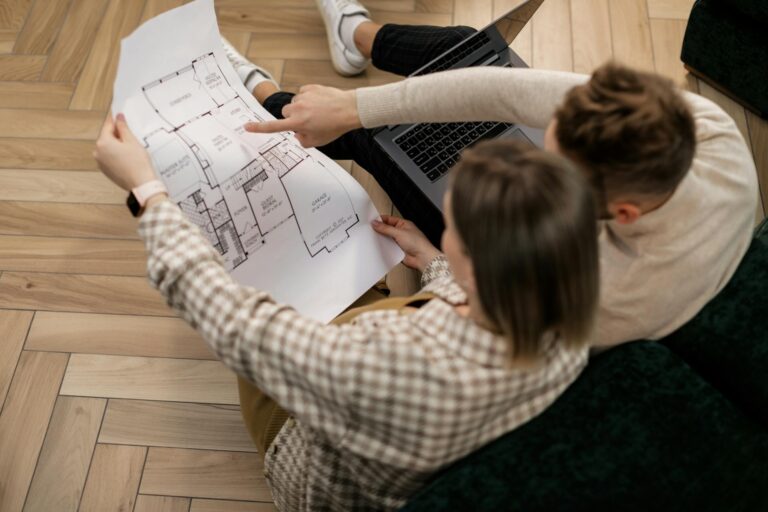 Couple sitting with plans on floor, laptop open - Design-Build vs. Traditional Remodeling