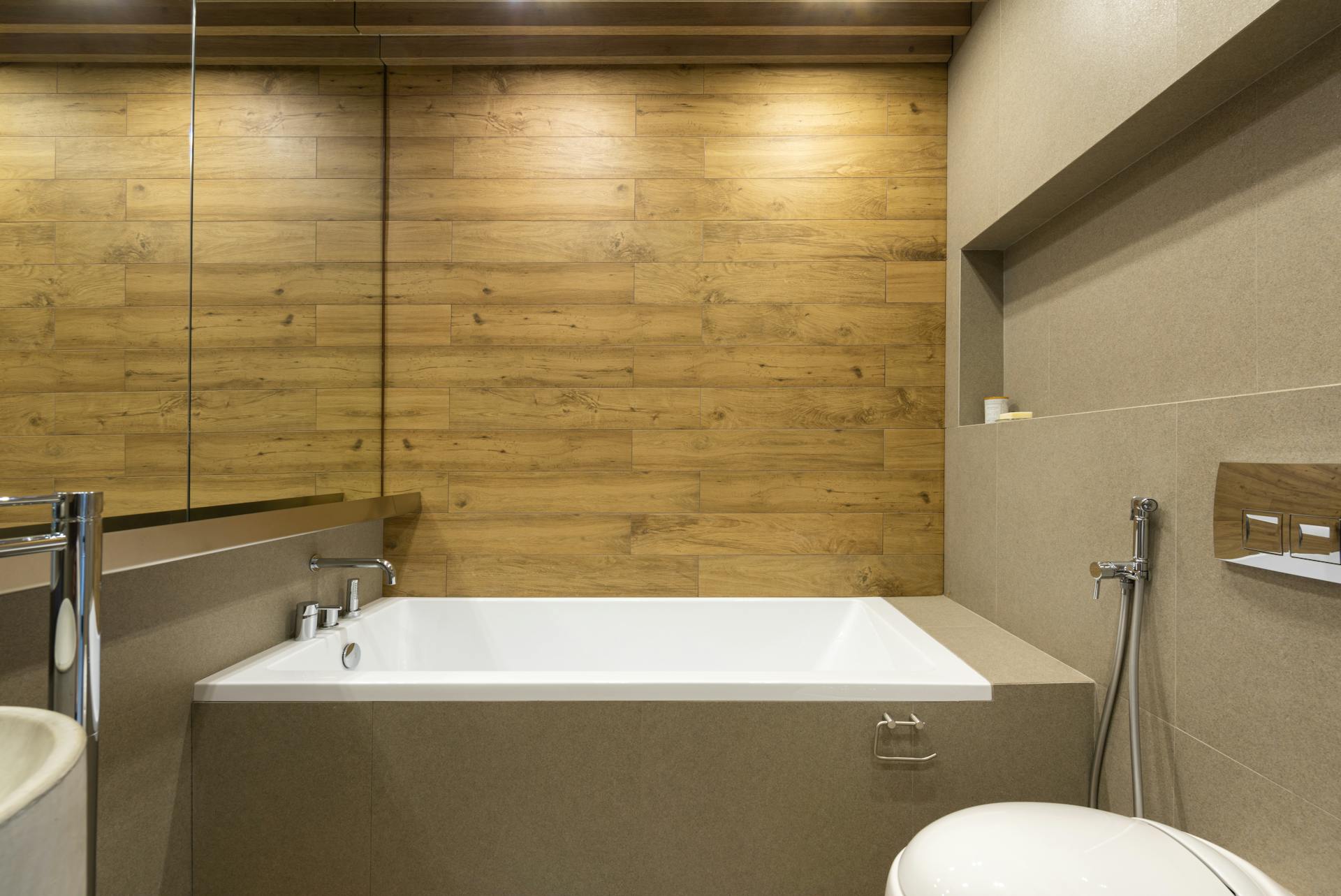 Modern soaking tub with integrated wood-look tile accent wall and recessed lighting for a warm, spa-inspired setting.