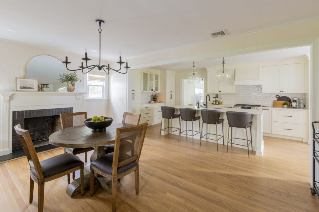 Open-concept kitchen remodeling with white cabinetry, large island with barstools, pendant lighting, and adjoining dining area with fireplace and wooden table - Kraftmaster Renovations NJ