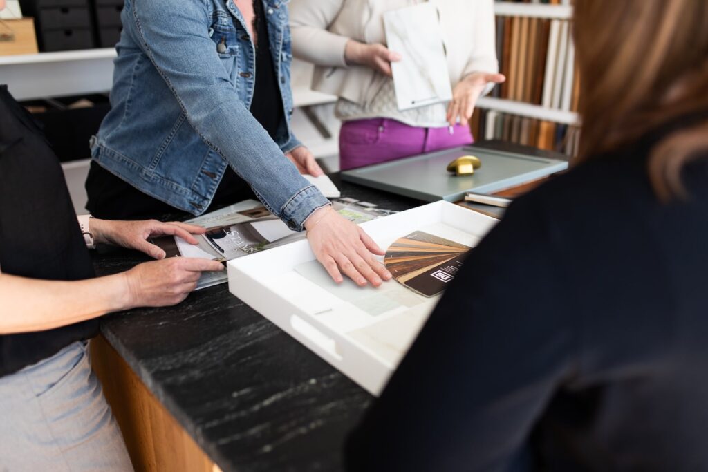Design team reviewing cabinetry finishes and material samples on a dark stone countertop during a kitchen planning session.