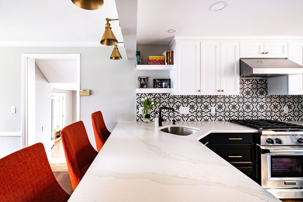 Close-up of kitchen backsplash and cabinetry pairing featuring white upper cabinets, black lower cabinets, brass hardware, and a black-and-white patterned tile backsplash.